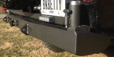 1979 Ford Bronco - A close-up, low-angle shot of a black aftermarket rear bumper on a vehicle. Visible features include tow hitch receivers, tie-down points,…