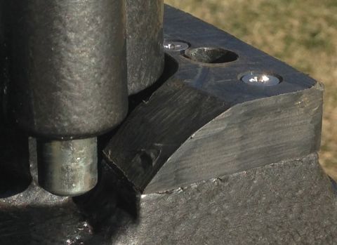 1979 Ford Bronco - A close-up view shows a dark metal part with a beveled edge and two circular indentations, one with a shiny screw head visible. The part ap…