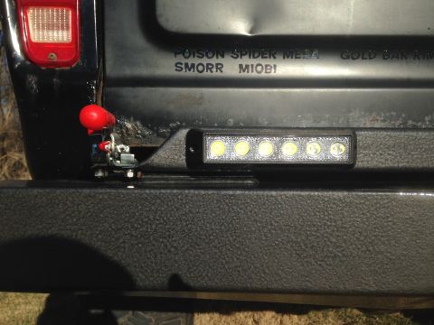 1979 Ford Bronco - The rear of a black SUV shows a red tow hook latch and a small LED light bar mounted on the aftermarket bumper. Text on the tailgate reads…
