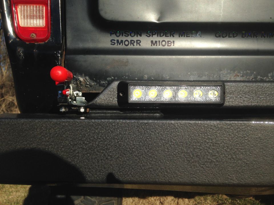 Black SUV rear with red tow hook latch and LED light bar on bumper. Tailgate has text.