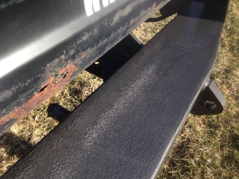 1979 Ford Bronco - A close-up view shows significant rust and peeling paint on the lower body panel of a vehicle, contrasted with a textured black aftermarket…