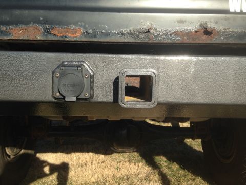 1979 Ford Bronco - A close-up view of the rear bumper of a vehicle, showing a 7-pin trailer connector and a trailer hitch receiver. The bumper is textured bla…