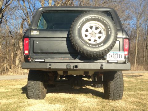 1979 Ford Bronco - The rear of a dark-colored Ford Bronco is shown, featuring a spare tire mounted on the back, a custom bumper, and an Iowa license plate tha…
