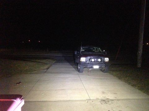 1979 Ford Bronco - A dark red pickup truck is parked on a concrete driveway at night. The truck has a large aftermarket bumper with auxiliary lights and is il…