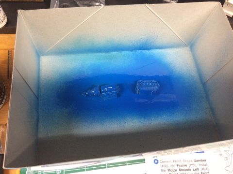 1989 Ford Bronco - Model engine parts are being spray painted blue inside a cardboard box, with instructions visible at the bottom.