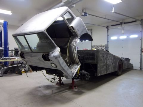 1989 Ford Bronco - Unfinished truck chassis with cab raised, revealing the bare metal frame and trailer bed in a workshop.