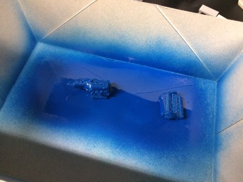 1989 Ford Bronco - Two blue engine parts are being spray painted inside a booth.