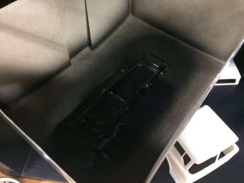 1989 Ford Bronco - A black model car chassis is being spray painted inside a cardboard booth.