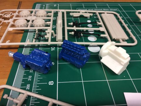 1989 Ford Bronco - Unassembled model engine parts, including blue painted V8 engines and white engine blocks, lie on a green cutting mat with rulers.