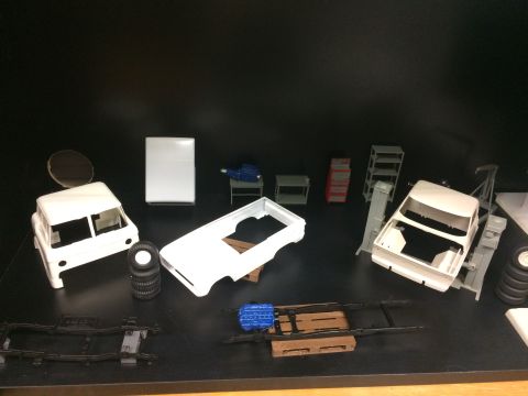 1989 Ford Bronco - Various unassembled model car parts, including a chassis, body, engine, and tires, are laid out on a black surface.