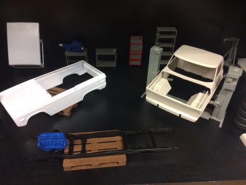 1989 Ford Bronco - Model car parts laid out on a black surface, including a truck bed, chassis, and engine.
