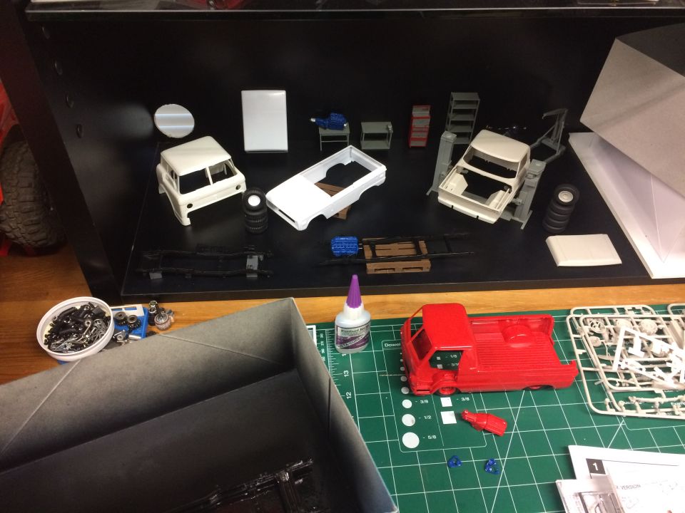 Model car parts and tools laid out on a table for assembly. Includes a red truck model and white truck/SUV models