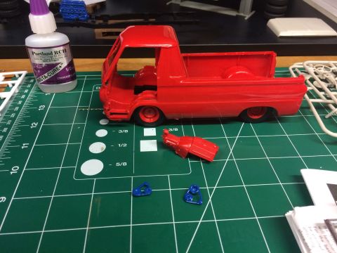 1989 Ford Bronco - Model truck parts laid out on a cutting mat, including a red truck body, detached engine, and blue components, alongside a bottle of glue.