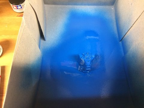 1989 Ford Bronco - A model car engine part is being spray painted blue inside a booth.