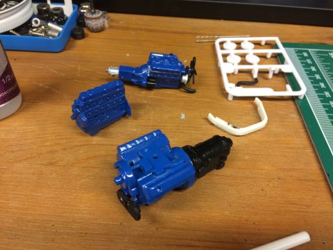1989 Ford Bronco - Model engine components, including a block and transmission, are laid out on a workbench next to a sprue and a bottle of glue.