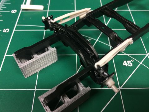 1989 Ford Bronco - Close-up of a model vehicle's chassis assembly, showing suspension components and a black frame on a cutting mat.