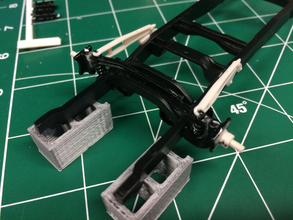 Model truck chassis with suspension parts on 3D printed blocks on a cutting mat.