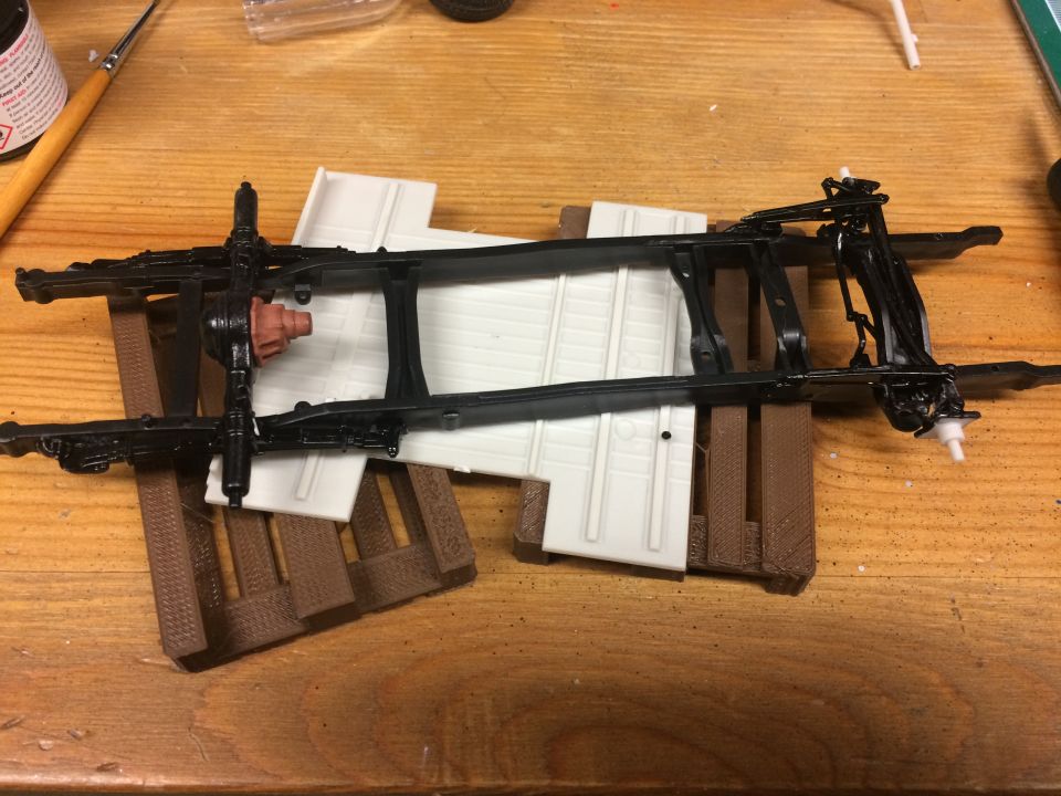 Model vehicle chassis with differential and suspension parts on a wooden table.