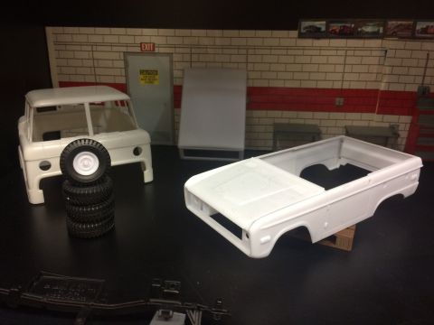 1989 Ford Bronco - A white plastic model of a Ford Bronco body sits on a wooden pallet next to a stack of model tires. In the background is a model garage sce…