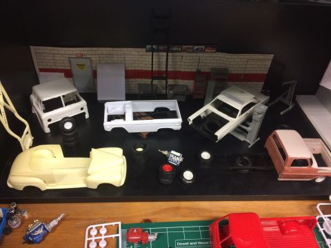 1989 Ford Bronco - A collection of unfinished model car kits, including several truck beds and car bodies, are displayed on a black surface with a brick wall…
