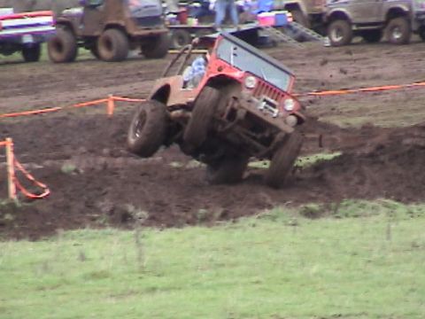 1994 Ford Explorer - A red off-road vehicle navigates a muddy course, with other vehicles visible in the background.