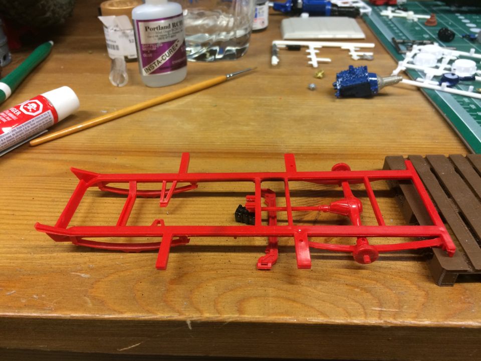 Red plastic model car chassis with suspension and drive train parts on a workbench.