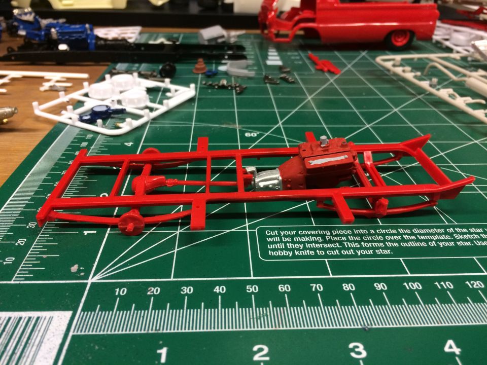 Red model truck chassis and engine on a green cutting mat.