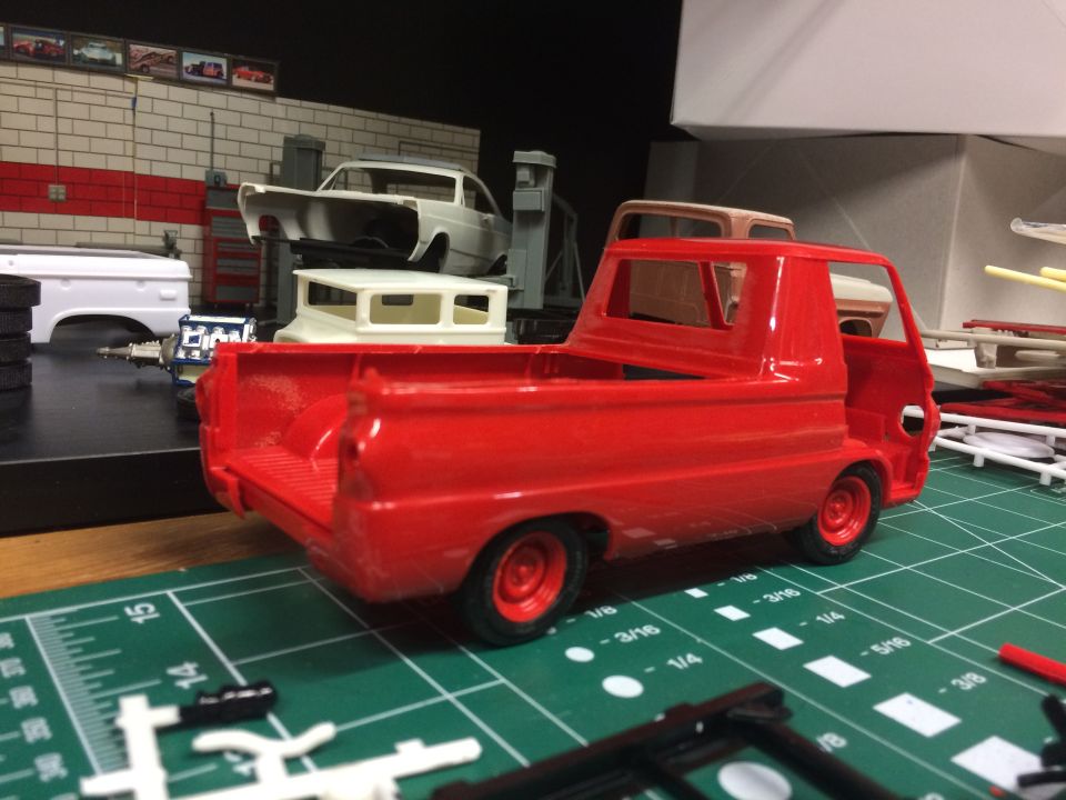 Red model pickup truck on a green cutting mat with model car parts in the background.