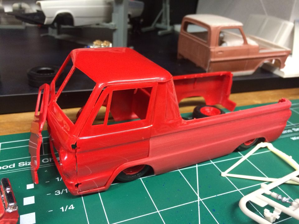 Red model pickup truck with detached door on a green cutting mat. Another model truck in background.