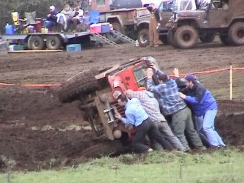 1994 Ford Explorer - Several people attempt to right a red Jeep that has overturned in a muddy area, with other vehicles and spectators present.