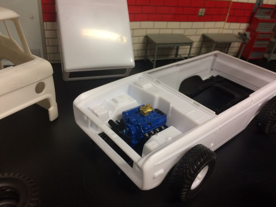 White plastic model truck body with blue engine and gold valve covers, front tires attached.
