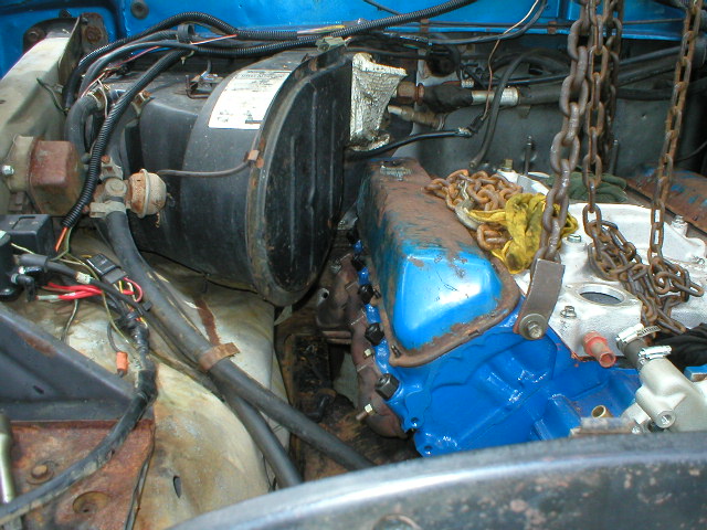 Blue Ford V8 being lifted into an engine bay on a chain hoist during a swap