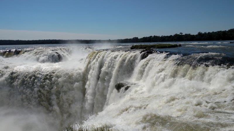 Wide waterfall cascading into mist below a clear sky