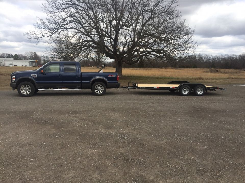 Dark blue Ford F-Series pickup truck towing a flatbed trailer.