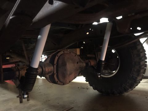 1982 Ford Bronco - The underside of a vehicle shows a rear differential with two white shock absorbers mounted on either side. A large, knobby tire is visible…