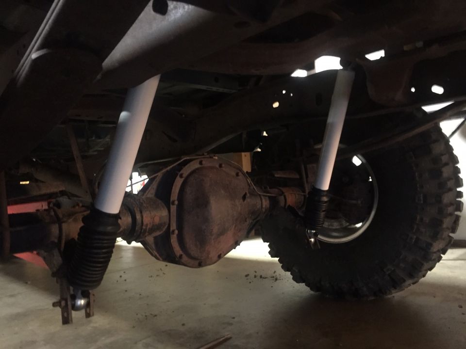 Underside of a vehicle showing rear differential and shock absorbers with a large tire.