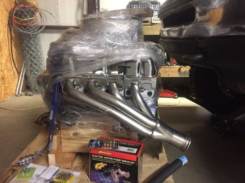 1982 Ford Bronco - A V8 engine wrapped in plastic wrap sits on a wooden pallet next to a portion of a dark-colored vehicle. Several boxes of automotive parts…