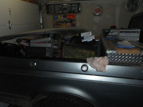 1995 Ford F-150 - The bed of a dark-colored pickup truck is filled with various items, including toolboxes, ammunition cans, and car parts. A diamond plate t…