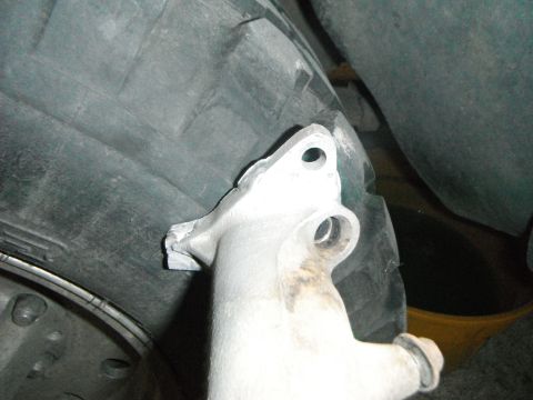 1995 Ford F-150 - Underbody view of a raw cast aluminum bracket with bolt holes mounted near a tire and inner fender.