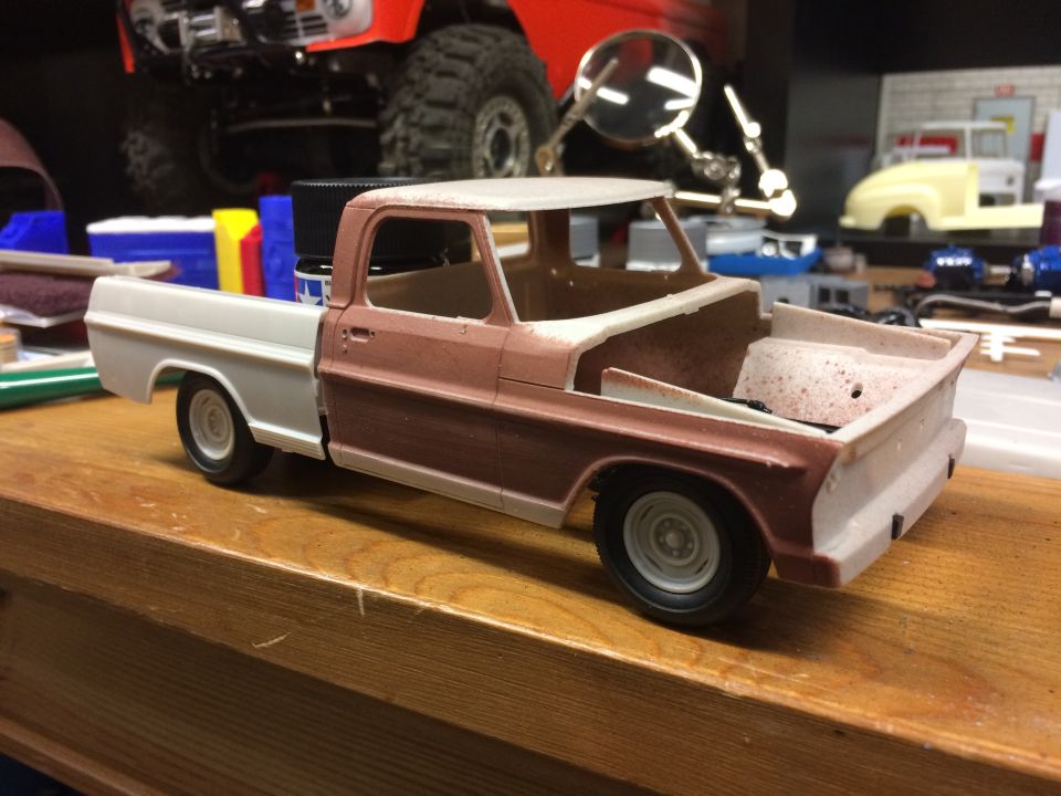 Model pickup truck with white cab and bed, brown lower body, on a wooden surface.