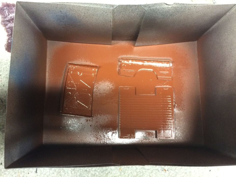 Plastic model car parts in a box, spray painted reddish-brown.