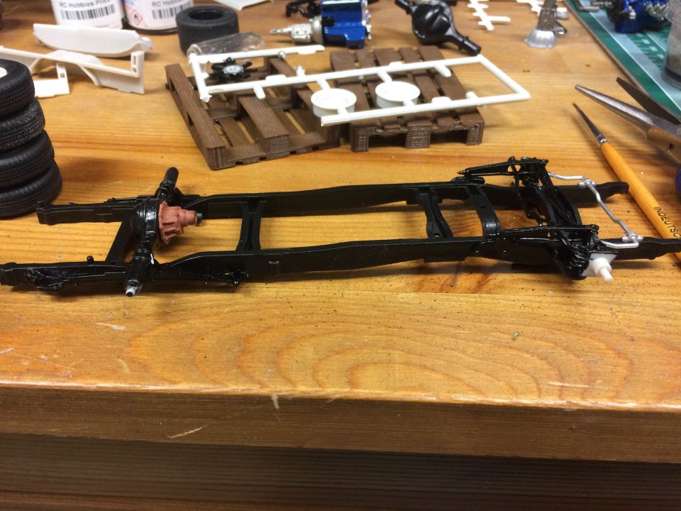 Model car chassis assembly with differential, tools, and parts on a wooden table.