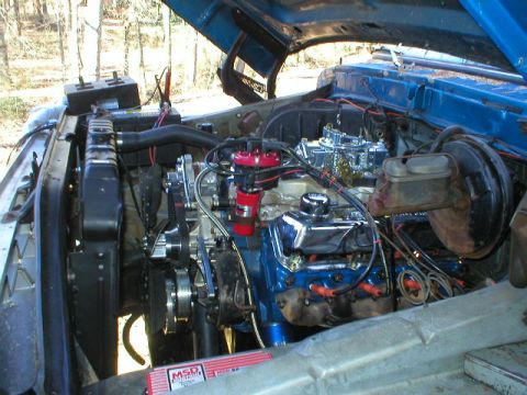 1978 Ford Bronco - Passenger-side view into a blue truck's engine bay showing a blue-block V8 with a four-barrel carburetor (air cleaner removed), red distrib…