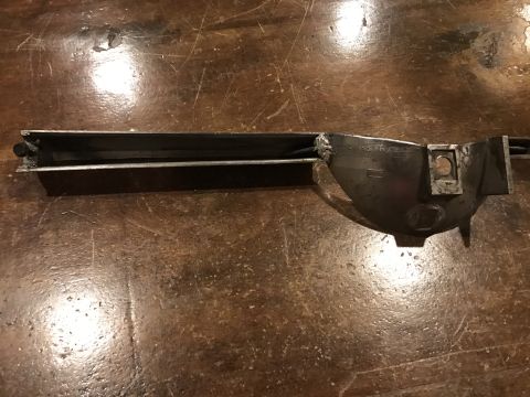 1965 Ford Mustang - A dark, metallic automotive part, possibly a bracket or housing, is shown lying on a wooden surface. The part has a rectangular channel on…