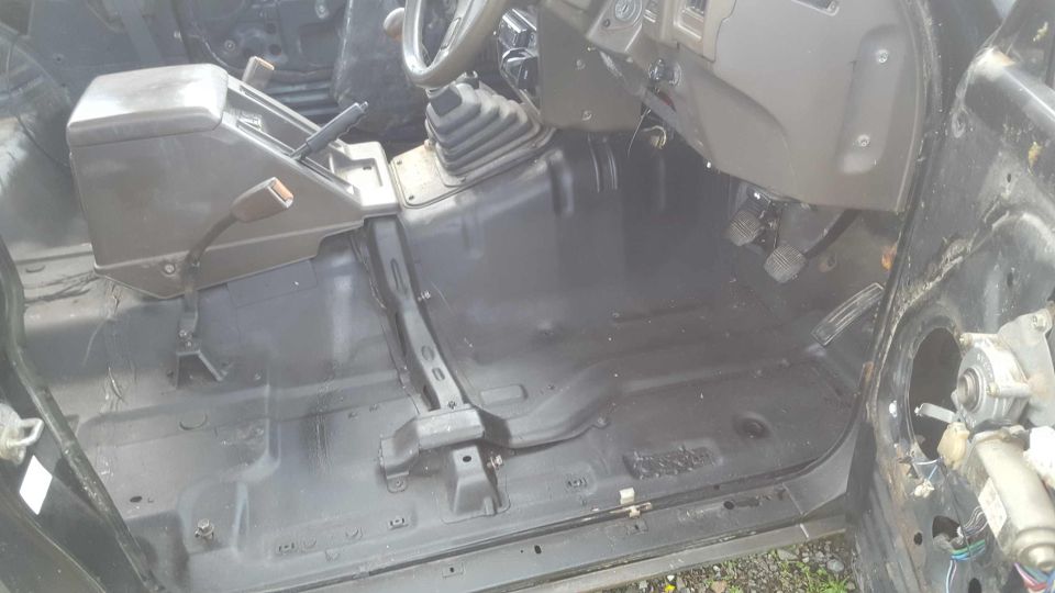 Interior of a vehicle with black painted floor, center console, gear shifters, and pedals.