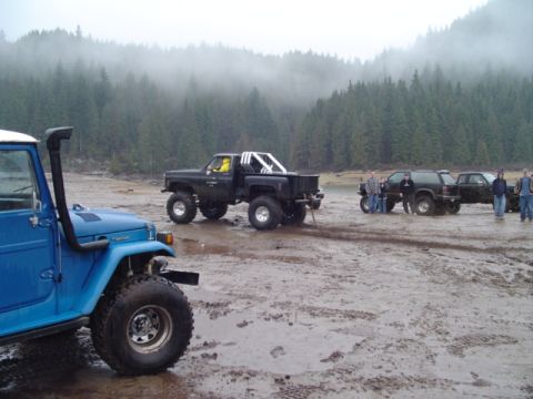 1993 Ford Bronco - Several off-road vehicles are parked on muddy ground near a forest with fog.