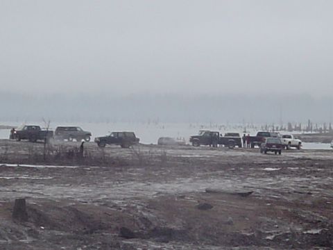 1993 Ford Bronco - A group of trucks and SUVs are parked in a muddy, open area with a hazy sky overhead.