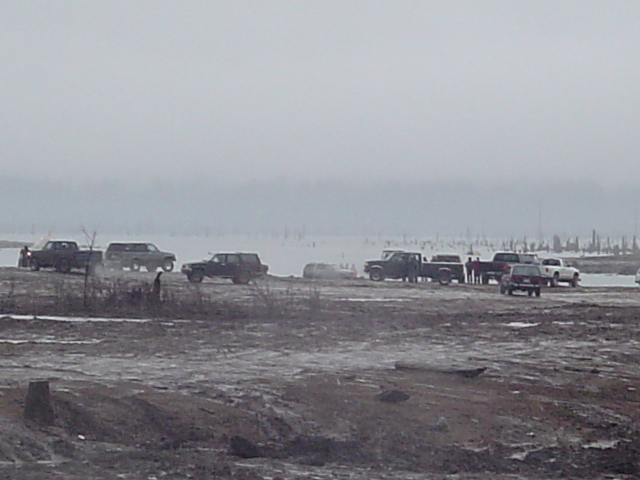 Several trucks and SUVs gathered in a muddy, desolate area under a hazy sky