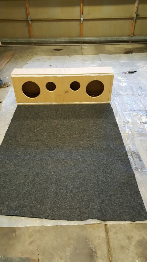 1996 Ford Bronco - A custom-built speaker box with four circular openings sits on a dark gray carpet. The speaker box is made of light-colored wood and is pos…