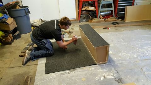 1996 Ford Bronco - A young man kneels on a carpeted surface, spraying a can of adhesive onto a wooden box with a carpeted top. He is in a garage or workshop s…